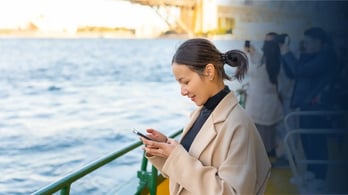Happy business woman using her cell phone to receive a reward on a boat in Sydney Harbour (Australia)