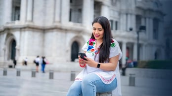 woman receiving something on her cell phone in front of blurred Bellas Fine Arts Palace in Mexico City