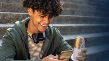 young man enjoying a Dunkin' donut and looking at his cell phone